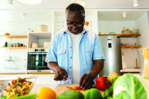 Image of black man cooking healthy meal while living with prostate cancer